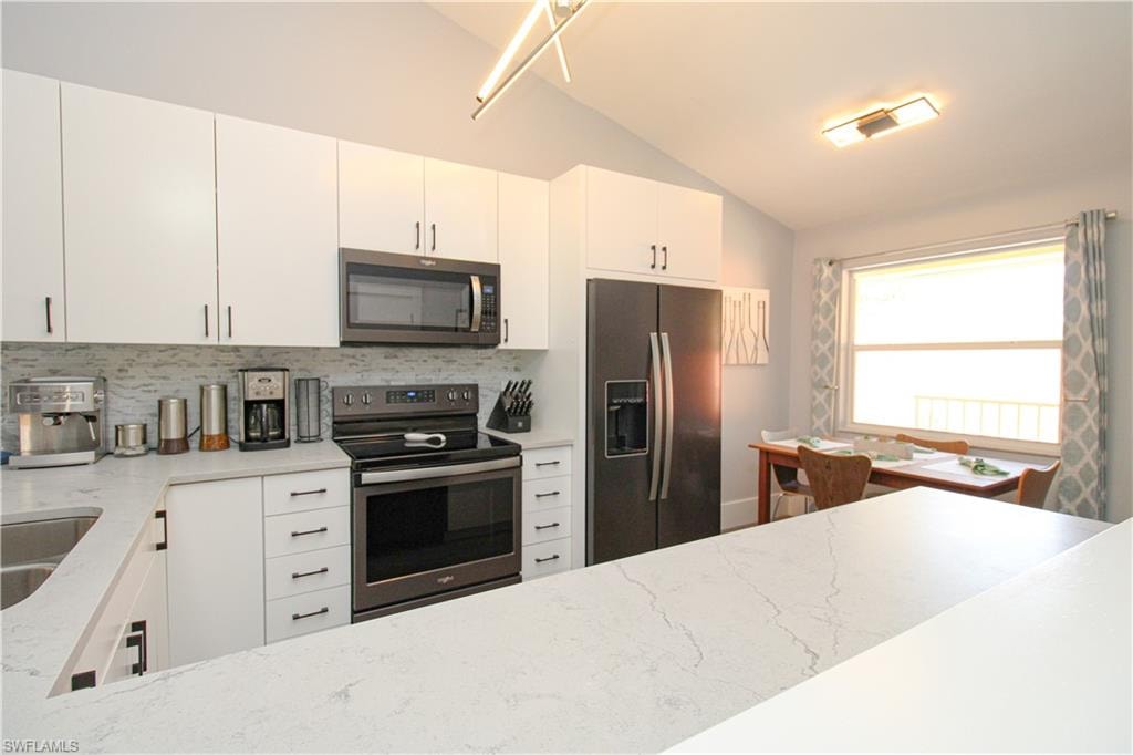 Kitchen featuring light stone counters, stainless steel appliances, tasteful backsplash, white cabinets, and lofted ceiling