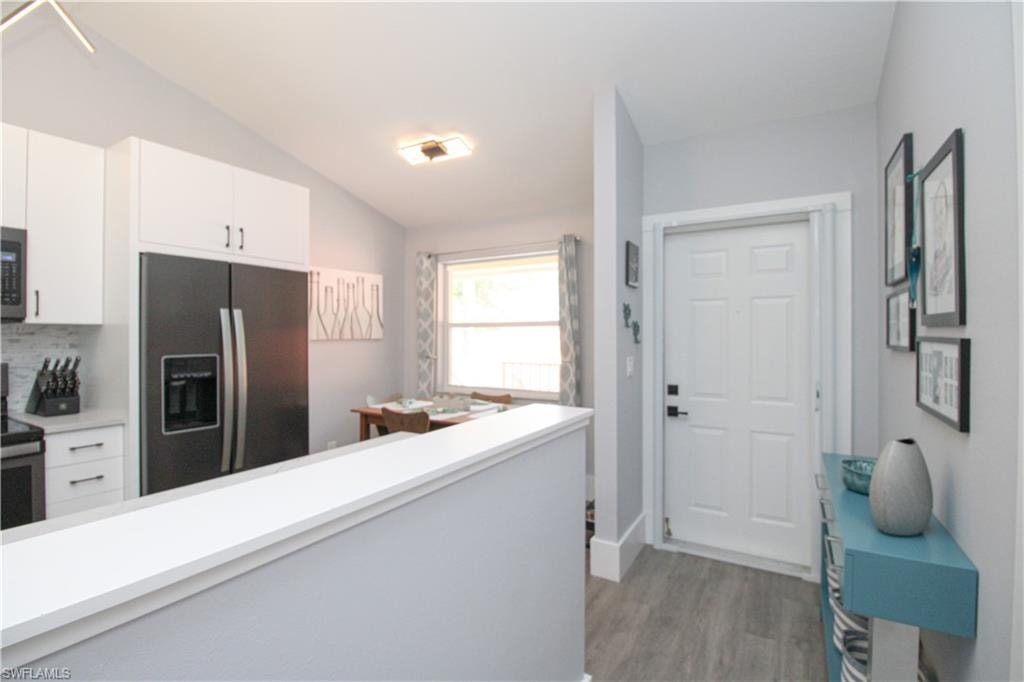 Kitchen featuring lofted ceiling, tasteful backsplash, wood-type flooring, white cabinets, and appliances with stainless steel finishes