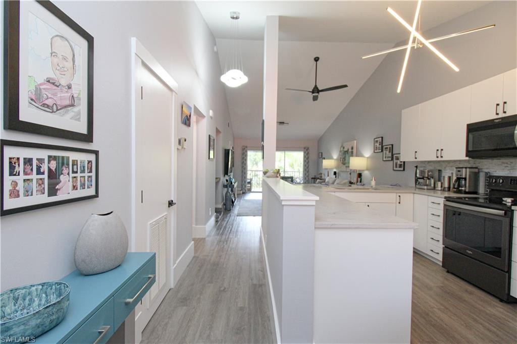 Kitchen with light hardwood / wood-style floors, hanging light fixtures, electric range oven, high vaulted ceiling, and white cabinets