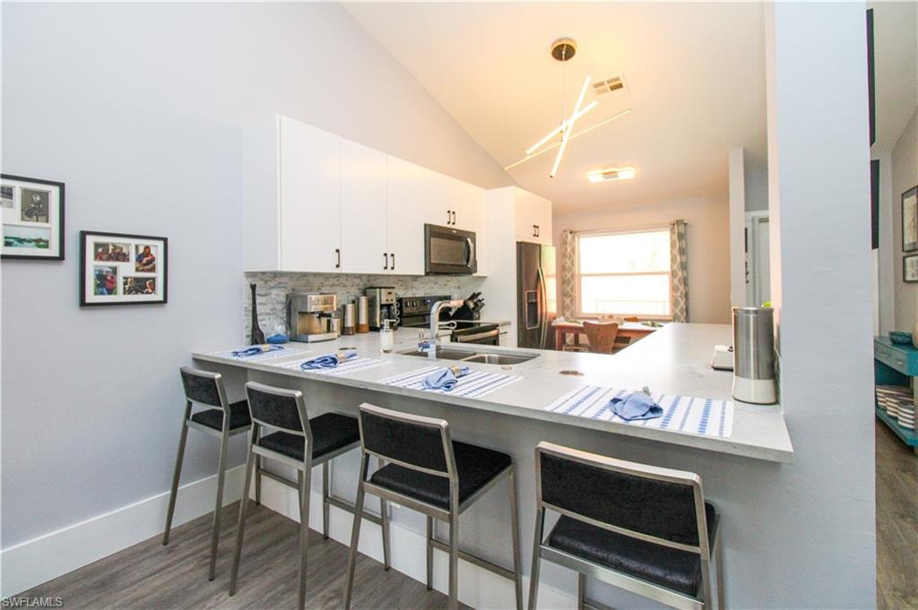 Kitchen with dark hardwood / wood-style flooring, stainless steel appliances, white cabinets, sink, and a breakfast bar