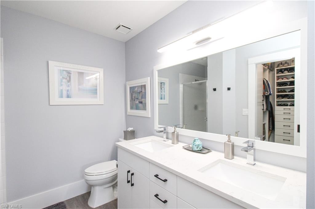 Bathroom with hardwood / wood-style floors, double sink, vanity with extensive cabinet space, walk in shower, and toilet