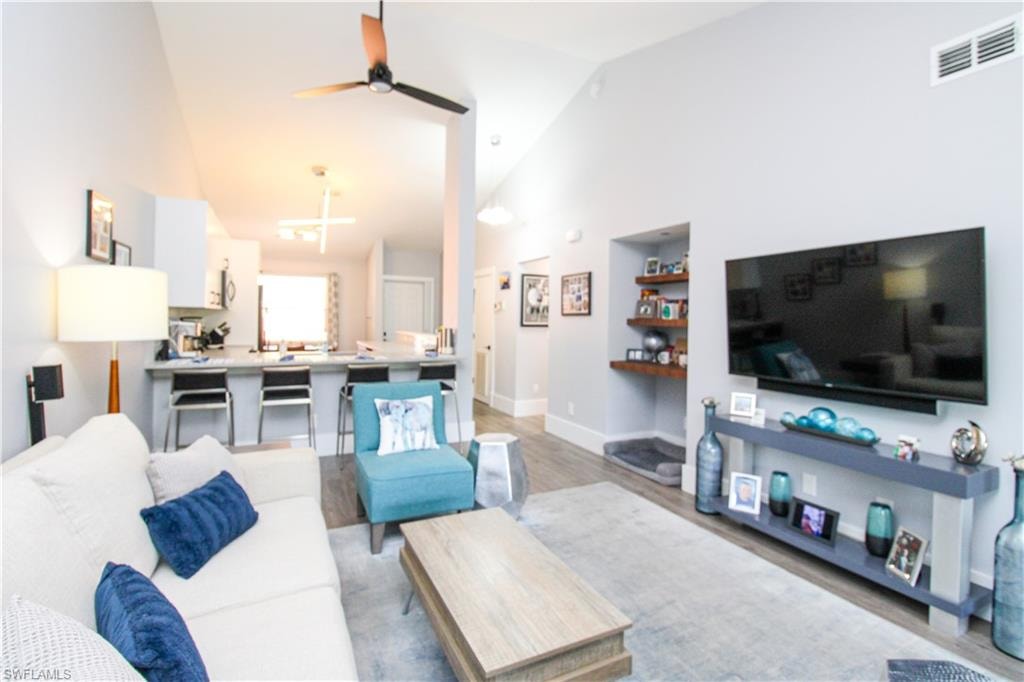 Living room featuring high vaulted ceiling, ceiling fan, and wood-type flooring