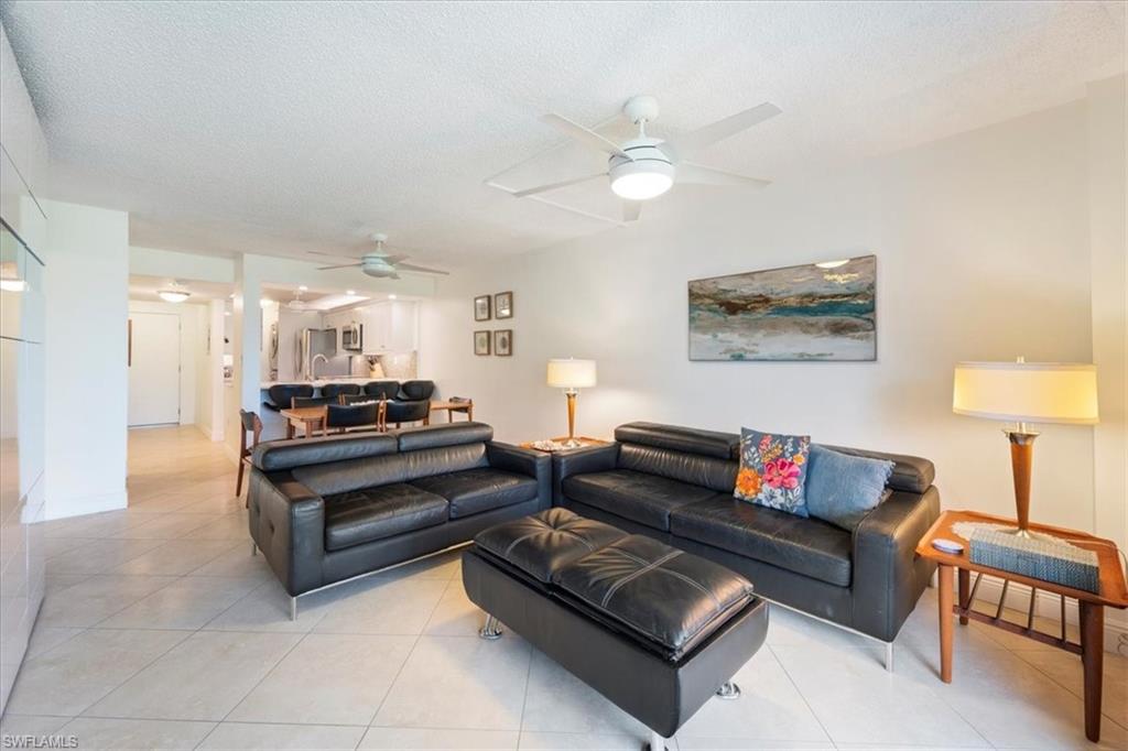 Living room with a ceiling fan, light tile patterned floors, and a textured ceiling