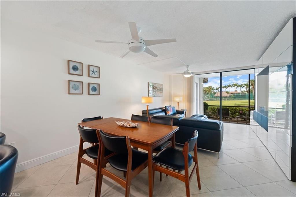 Dining space with a wall of windows, light tile patterned flooring, and a ceiling fan
