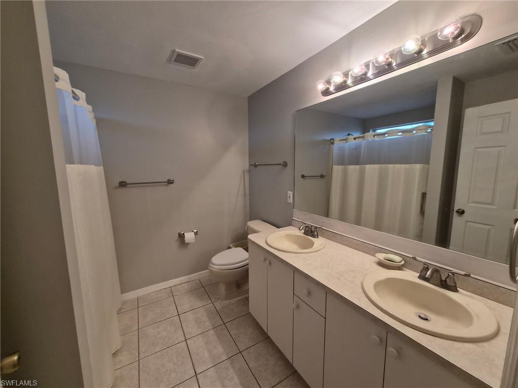 Full bathroom with double vanity, a shower with shower curtain, and light tile patterned floors