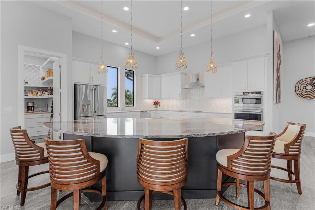 Kitchen with white cabinets, wall chimney exhaust hood, stainless steel appliances, and a large island
