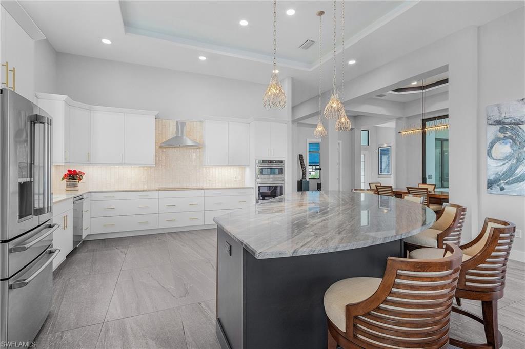 Kitchen with wall chimney range hood, white cabinetry, stainless steel appliances, and a tray ceiling