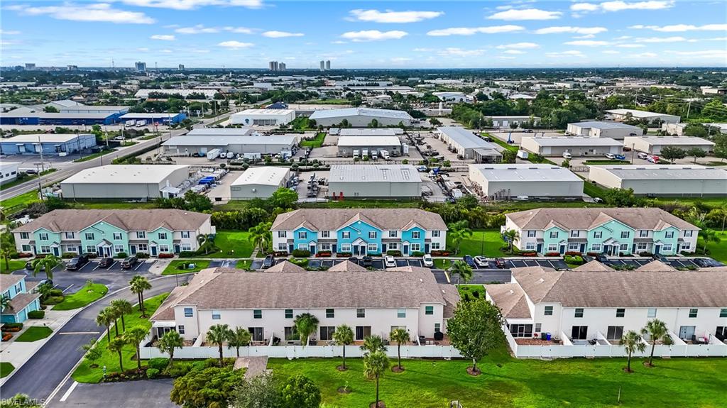 Aerial perspective showcasing multiple townhouse buildings with light-colored exteriors and dark roofing, surrounded by green lawns and mature palm trees