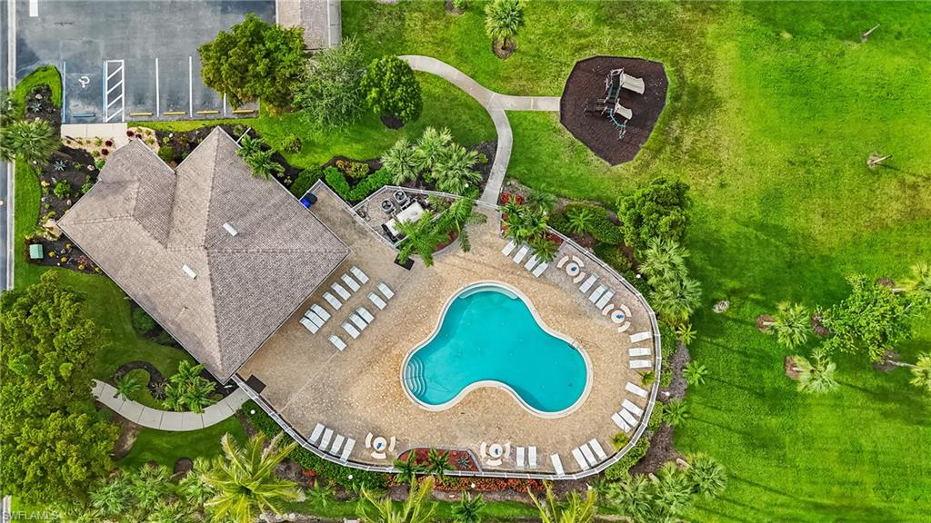 Resort-style pool area featuring a freeform swimming pool, extensive deck with multiple chaise lounges, and surrounding tropical landscaping