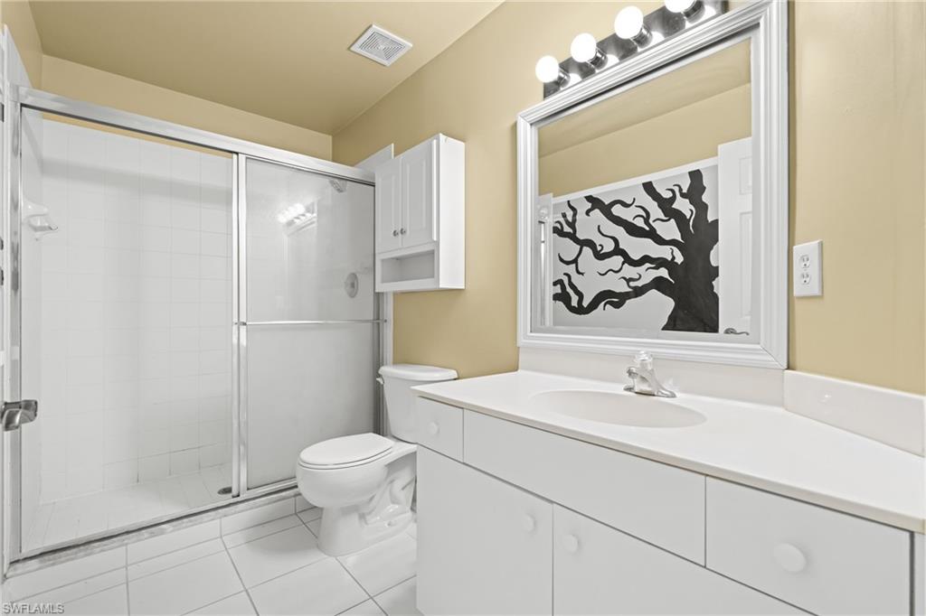 Bathroom featuring a white tile shower with sliding glass doors, a single vanity with an integrated sink, a large framed mirror, and upper wall cabinetry