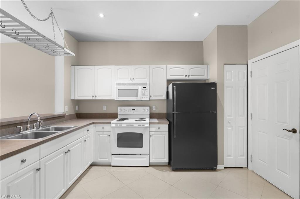 Kitchen featuring white cabinetry, a double basin stainless steel sink, a black refrigerator, a white electric range, and a built-in microwave