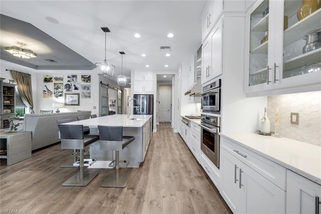 Contemporary kitchen featuring white cabinetry, integrated stainless steel appliances, a center island with seating, pendant lighting, and wood-finish flooring