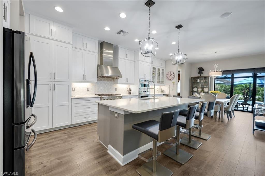 Modern kitchen featuring white cabinetry, a large center island with seating, stainless steel appliances, and wood-finish flooring