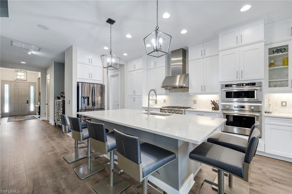 Gourmet kitchen featuring a large central island with seating, stainless steel appliances, white cabinetry, integrated double ovens, and wood-finish flooring