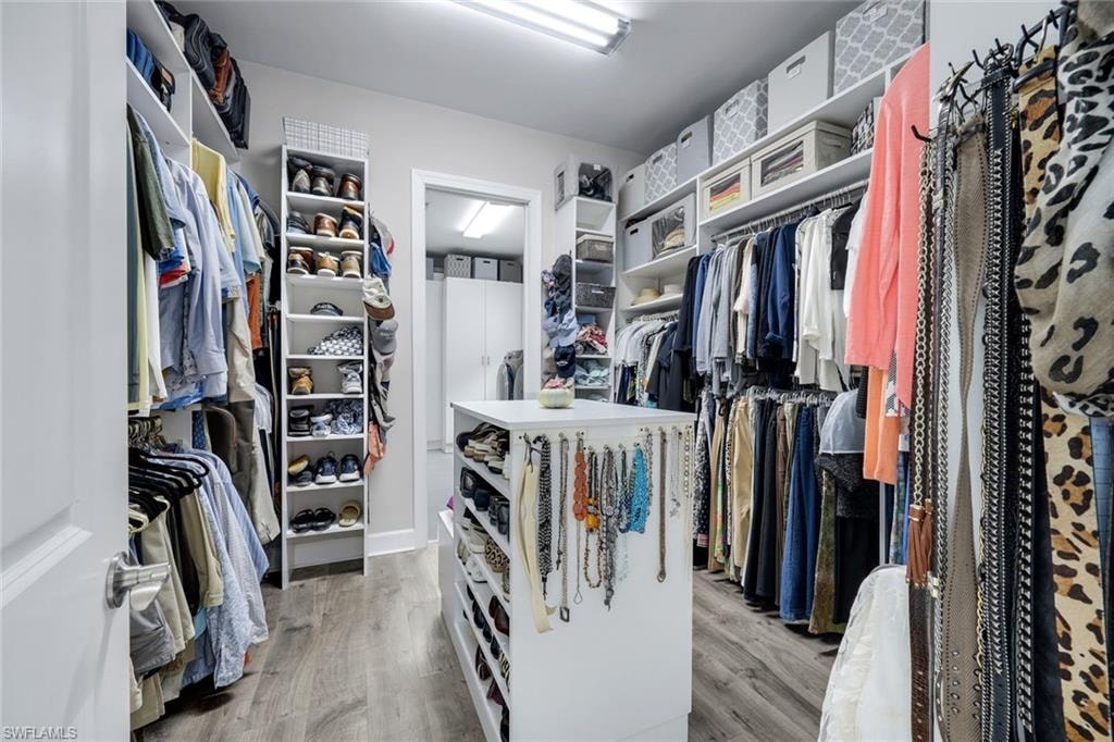 Spacious closet featuring wood-finish flooring, extensive built-in shelving, multiple hanging rods, and a central island with integrated storage