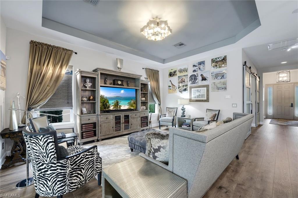 Spacious living area featuring wood-finish flooring, a tray ceiling, and a contemporary flush-mount light fixture