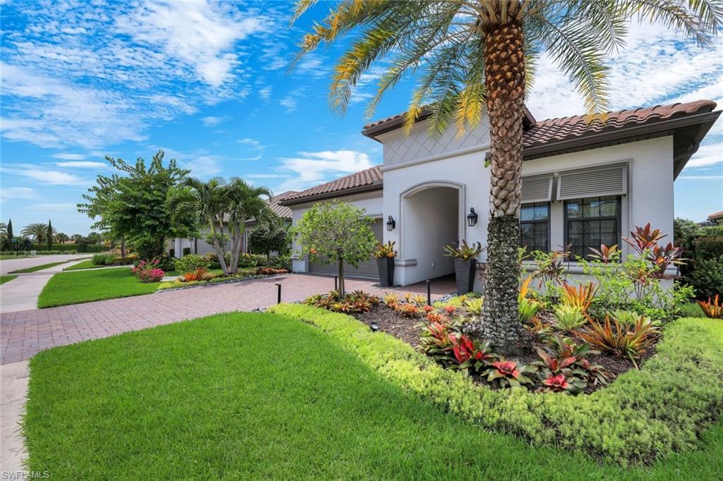 Exterior stucco residence featuring a tile roof, decorative entryway, paver driveway, and varied landscaping