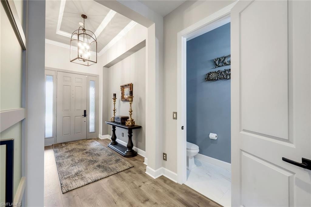 Foyer featuring a coffered ceiling, a decorative caged chandelier, wood-finish flooring, a paneled entry door with sidelights, and access to a powder room