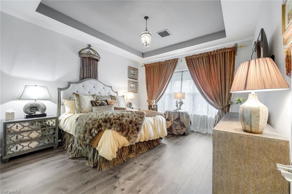 Bedroom featuring wood-finish flooring, a tray ceiling with recessed lighting, and a chandelier