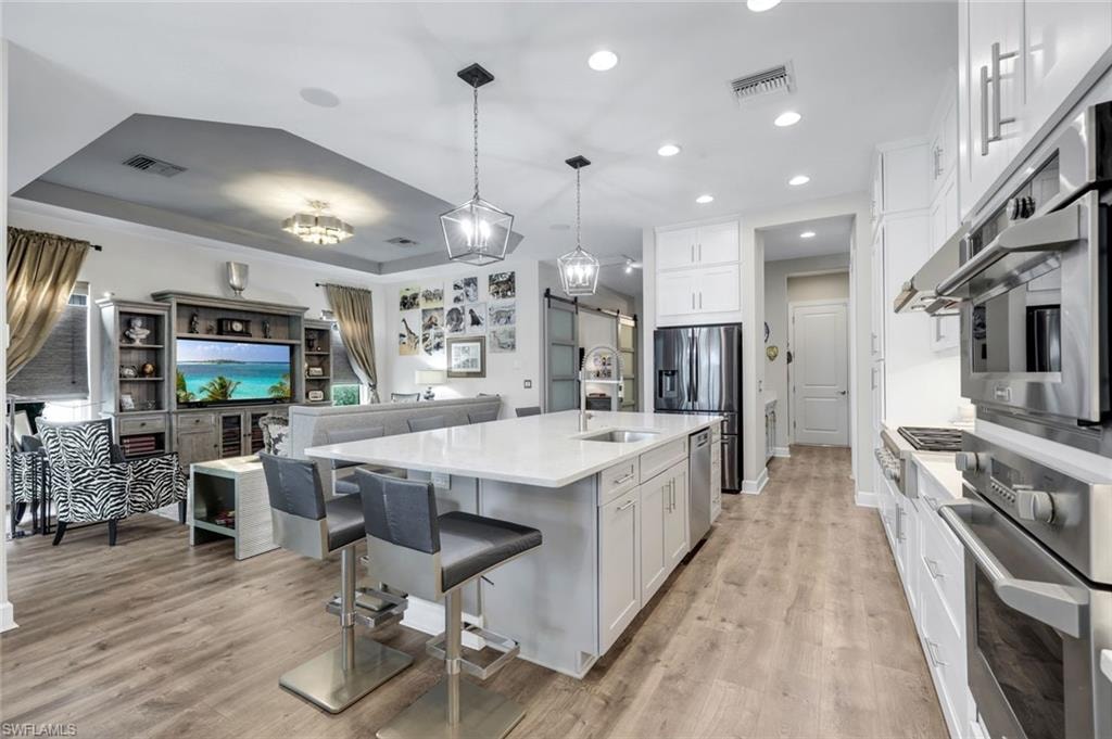 Open-concept kitchen with a large central island, light wood-finish flooring, white cabinetry, stainless steel appliances, and recessed lighting