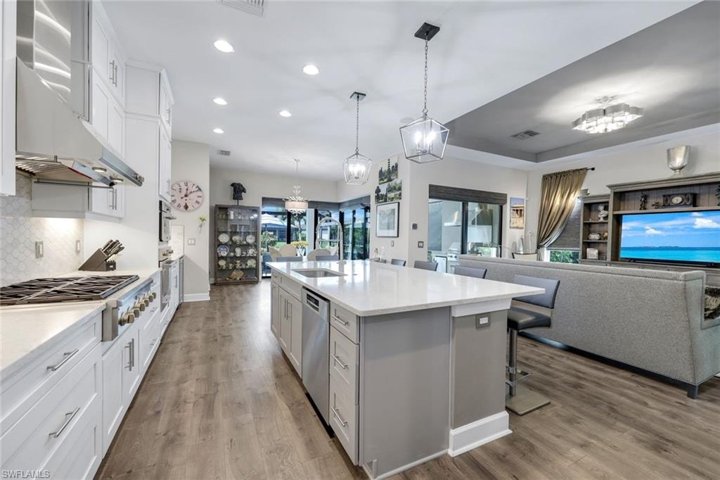 Open-concept kitchen featuring white cabinetry, a large kitchen island with countertop seating, stainless steel appliances, and wood-finish flooring