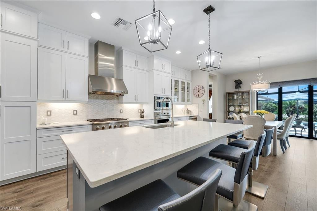 Modern kitchen featuring a large center island with seating, white shaker cabinetry, stainless steel appliances, and wood-finish flooring
