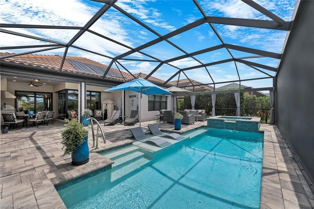 Screened lanai featuring a rectangular swimming pool with steps, an integrated spa with stone-look tile surround, and an expansive paver patio