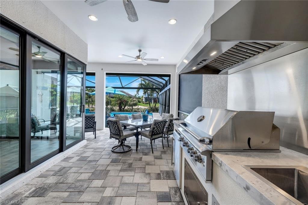 Expansive covered patio featuring patterned tile flooring, a built-in stainless steel grill with a large vent hood, and a stone-finish countertop with an integrated sink