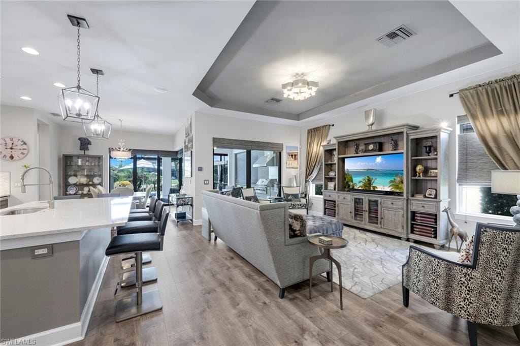 Open-concept living space featuring wood-finish flooring, a tray ceiling, and crown molding