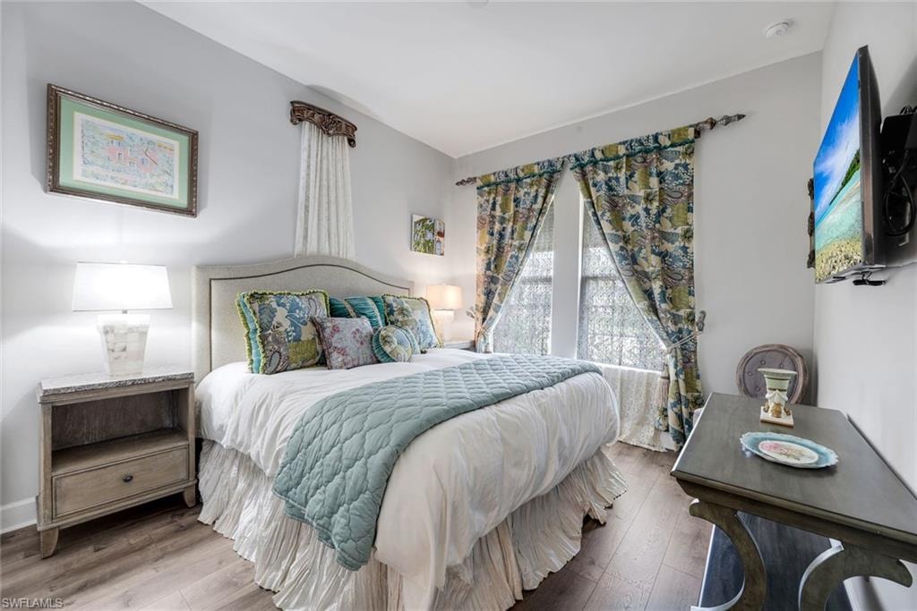 Bedroom featuring wood-finish flooring, light gray walls, and large windows with decorative drapery