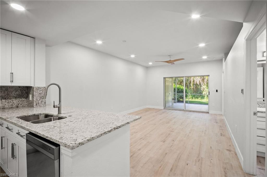 Kitchen featuring white cabinetry, backsplash, light stone countertops, stainless steel dishwasher, and recessed lighting