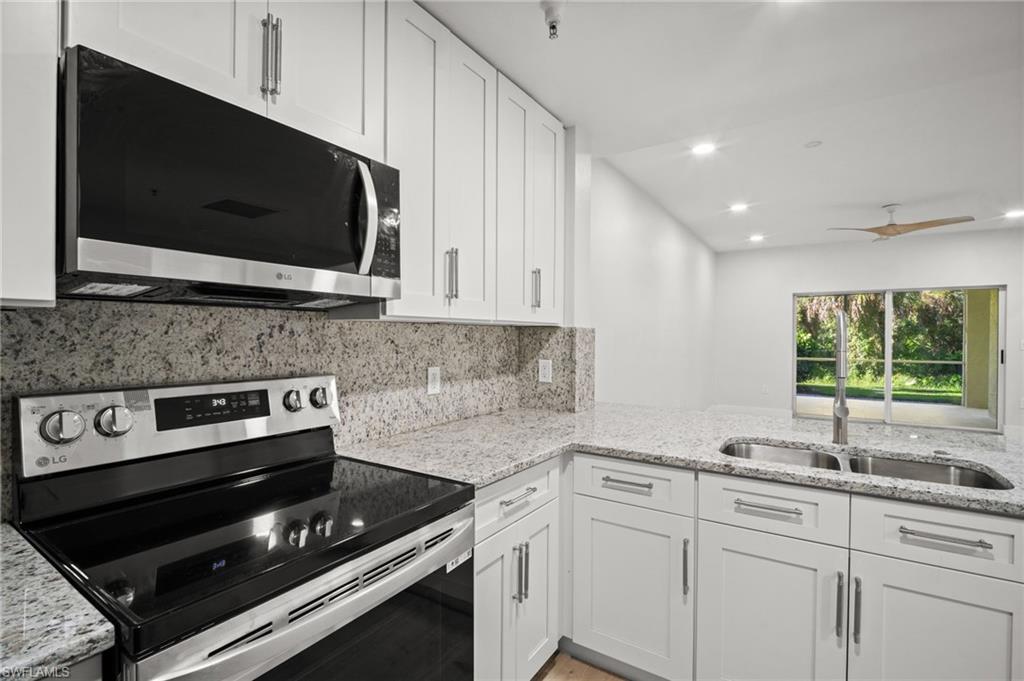Kitchen with appliances with stainless steel finishes, light stone countertops, white cabinets, and recessed lighting