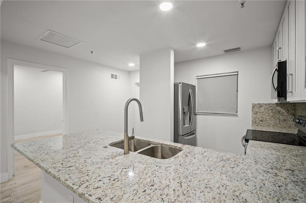 Kitchen featuring light stone countertops, white cabinets, stainless steel appliances, a peninsula, and light wood-style floors