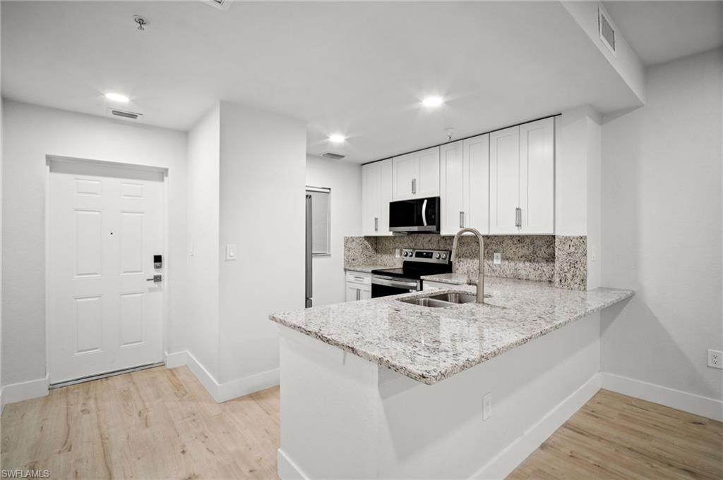 Kitchen featuring a peninsula, white cabinetry, light stone counters, stainless steel appliances, and backsplash