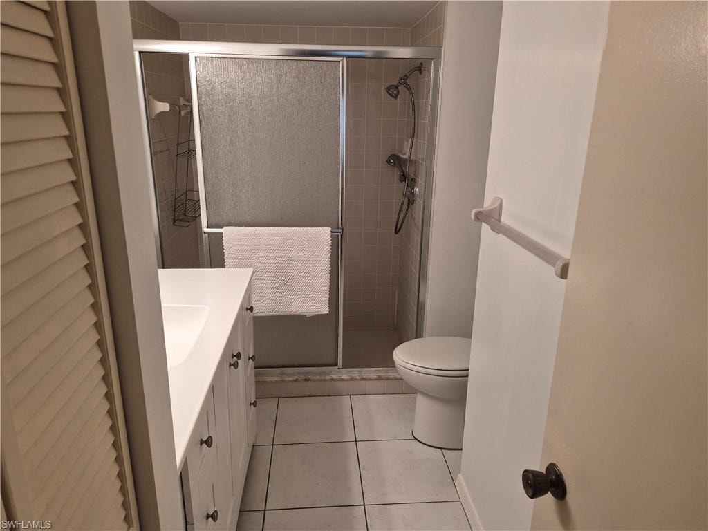 Bathroom featuring a shower with sliding glass doors, white vanity with integrated sink, white base cabinetry with dark hardware, and a tile floor