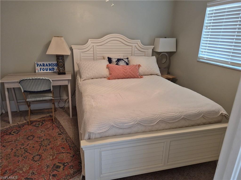 Carpeted room featuring a window with horizontal blinds, a light-colored desk, and a decorative area rug