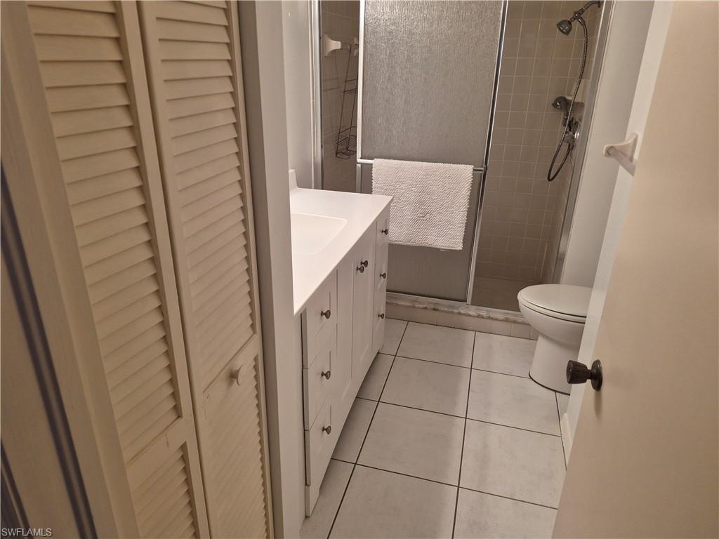 Bathroom featuring a white vanity with integrated sink, white tile flooring, a glass-enclosed shower with tiled walls, and louvered bi-fold closet doors