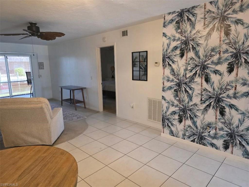 White tile flooring extending through the living space, a feature wall with palm frond wallpaper, and a ceiling fan with dark wood-finish blades