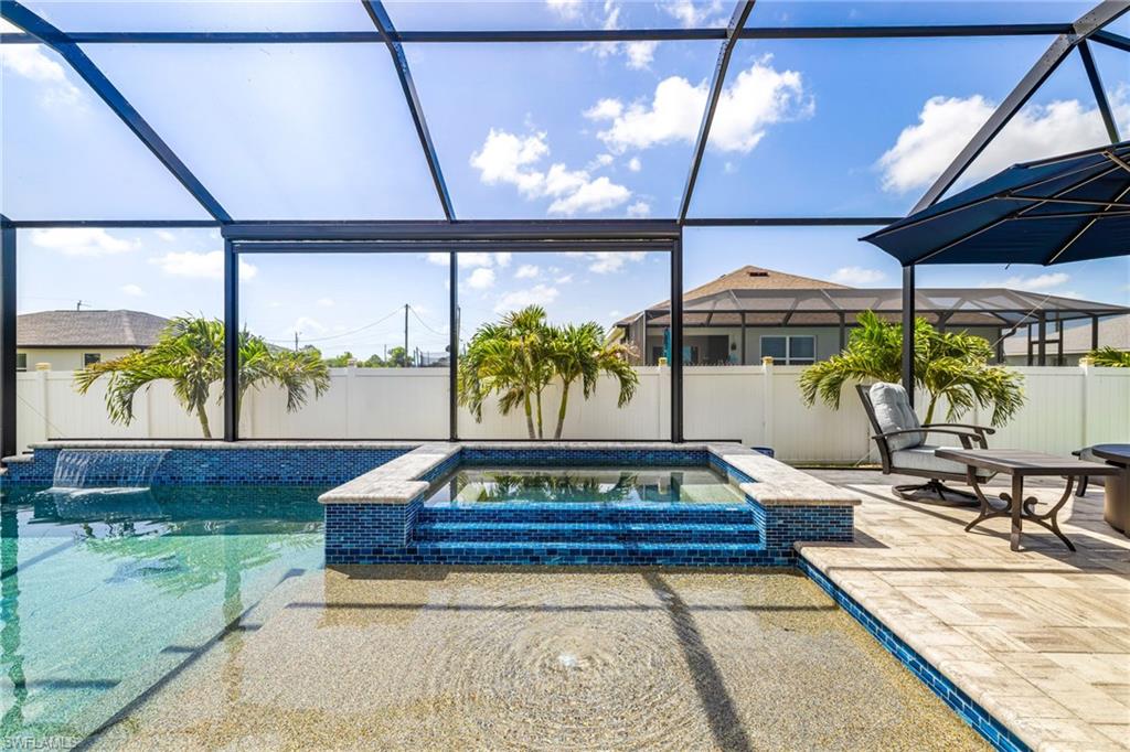 Screened lanai featuring a multi-level pool with a spa, blue mosaic tile accents, and a textured pool deck