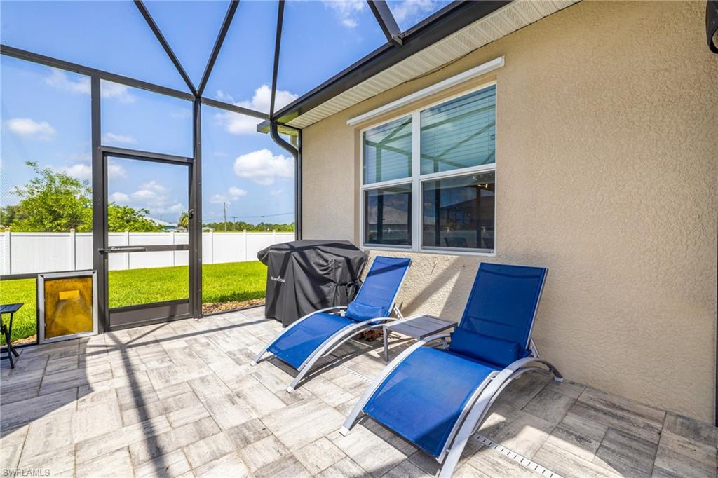 Screened patio featuring large format rectangular pavers, a stucco exterior, and a white privacy fence