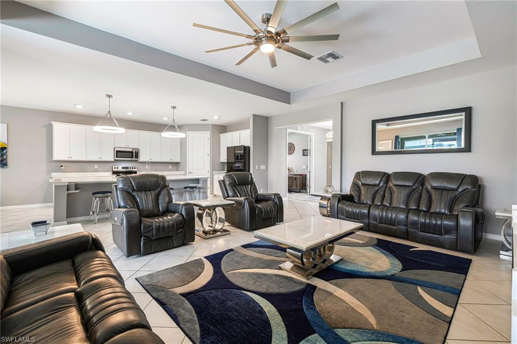 Open-concept living space featuring a tray ceiling with a contemporary ceiling fan, tile flooring, and light gray wall tones