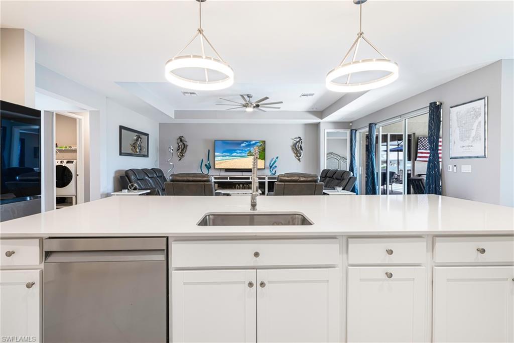 Expansive kitchen island featuring a stainless steel undermount sink, integrated dishwasher, and white shaker-style cabinetry with circular hardware