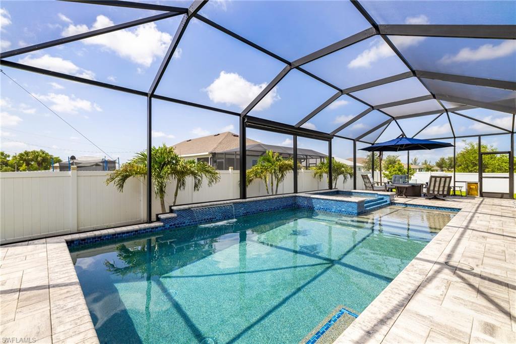 Screened pool enclosure featuring a custom-shaped pool, integrated spa, and paver decking
