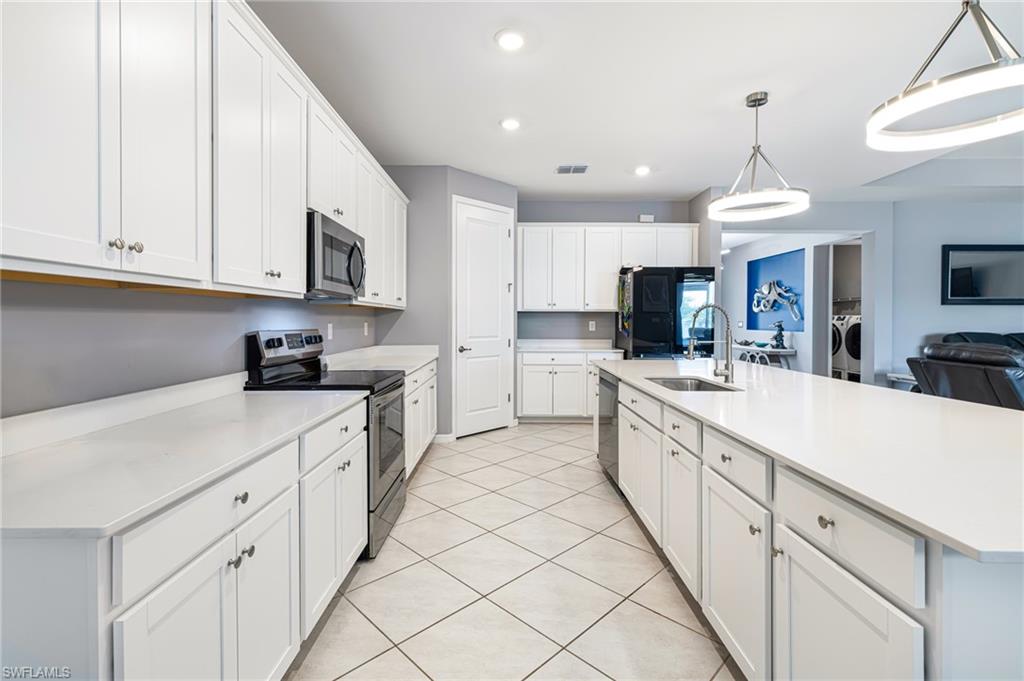 Spacious kitchen featuring white cabinetry, light countertops, stainless steel appliances, a large island with sink, and overhead pendant lighting