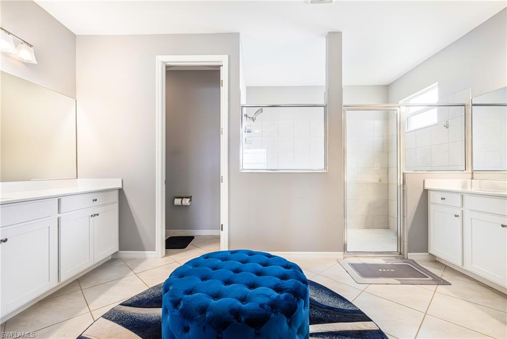 Bathroom featuring dual vanity areas with white cabinetry and light countertops, a glass-enclosed shower with tiled walls, and light-toned tile flooring