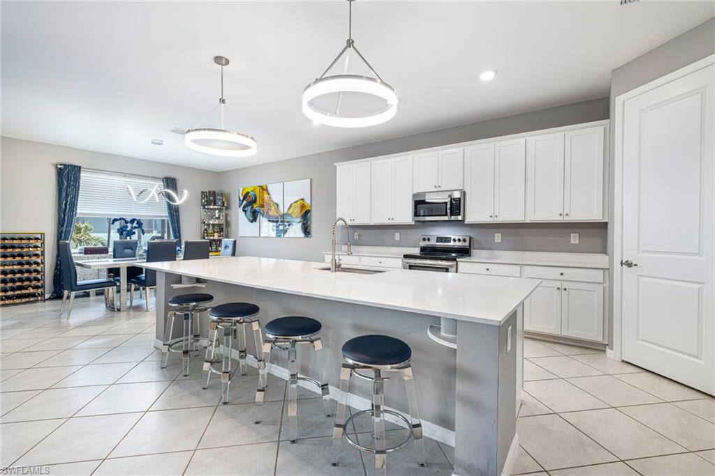 Expansive kitchen island with seating, white shaker cabinetry, stainless steel appliances, and tile flooring