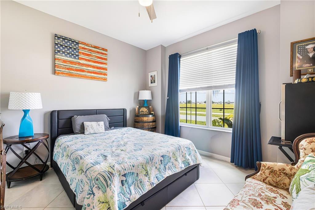 Spacious room with white tile flooring, a large window featuring white blinds and blue drapes, and a ceiling fan
