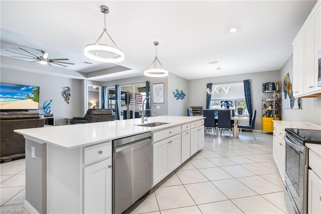 Spacious open-concept kitchen featuring a large central island with a sink and stainless steel dishwasher, white cabinetry, and light-toned countertops