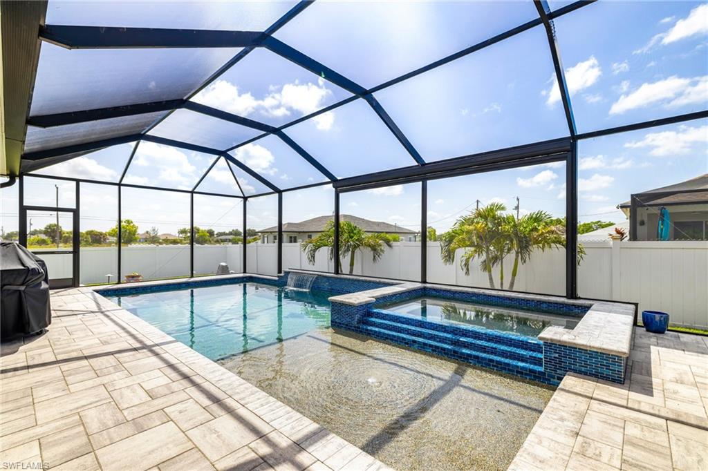 Screened outdoor living space featuring a swimming pool, integrated hot tub with mosaic tile, and a waterfall feature