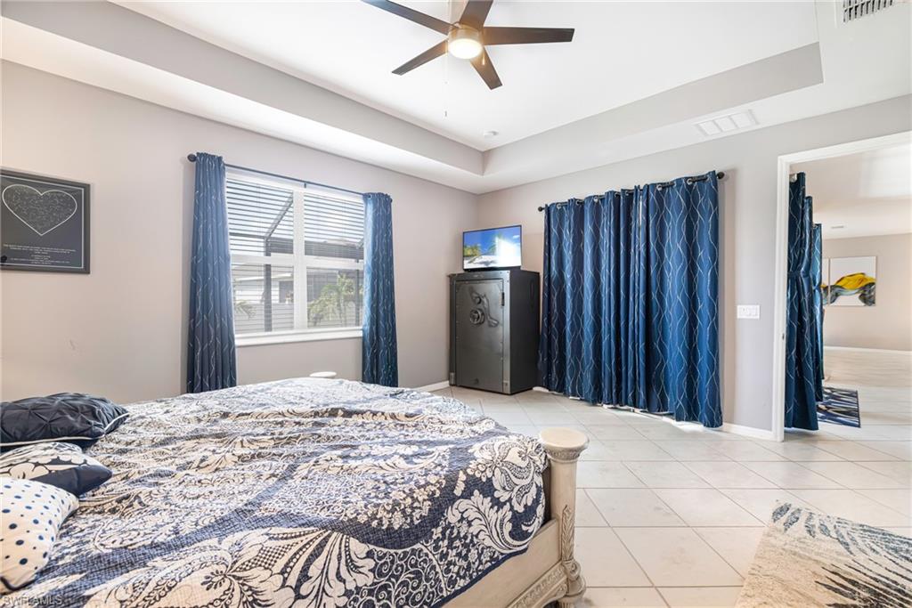 Spacious room featuring tile flooring, a tray ceiling with a ceiling fan, and a large window with horizontal blinds